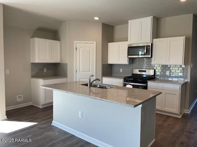 kitchen featuring a kitchen island with sink, stainless steel appliances, a sink, white cabinets, and light stone countertops