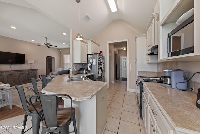 kitchen with ceiling fan, sink, decorative light fixtures, stainless steel refrigerator, and a breakfast bar