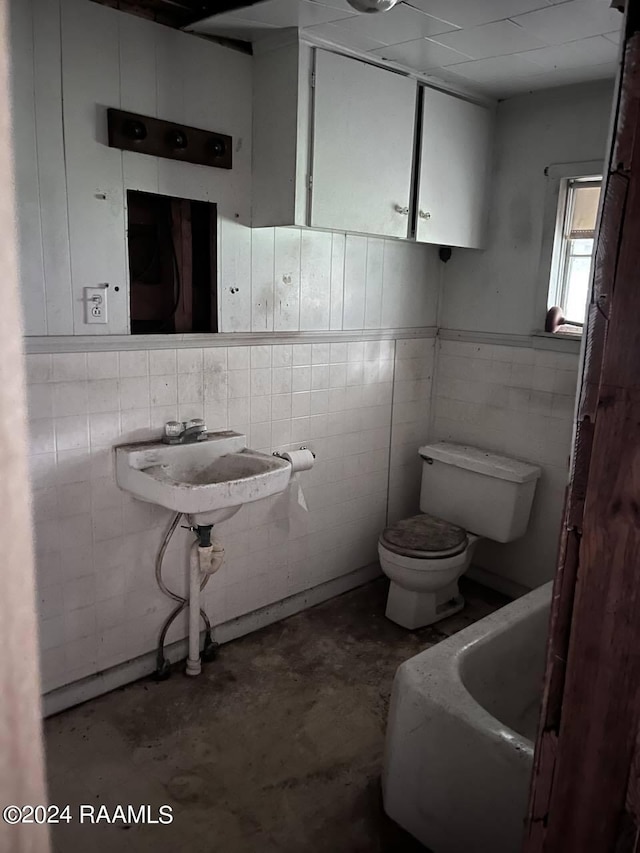 bathroom with sink, a tub, concrete floors, tile walls, and toilet