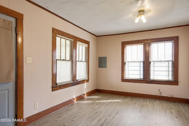 empty room featuring electric panel, light wood-type flooring, ornamental molding, and a healthy amount of sunlight