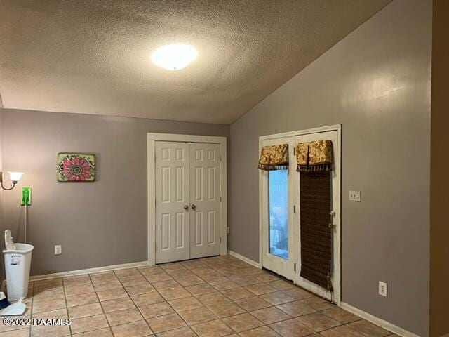 interior space with a textured ceiling, lofted ceiling, and light tile patterned floors