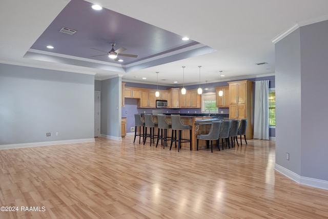 kitchen with pendant lighting, light wood-type flooring, a tray ceiling, ceiling fan, and ornamental molding