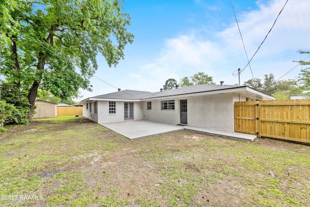 rear view of property featuring a lawn, a patio, and a shed