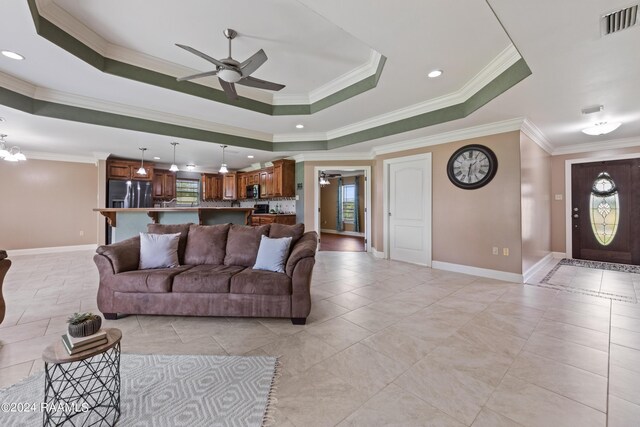 living room featuring ornamental molding, a raised ceiling, ceiling fan with notable chandelier, and a healthy amount of sunlight