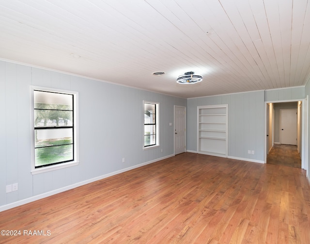 spare room with a healthy amount of sunlight, built in shelves, wood ceiling, and wood-type flooring