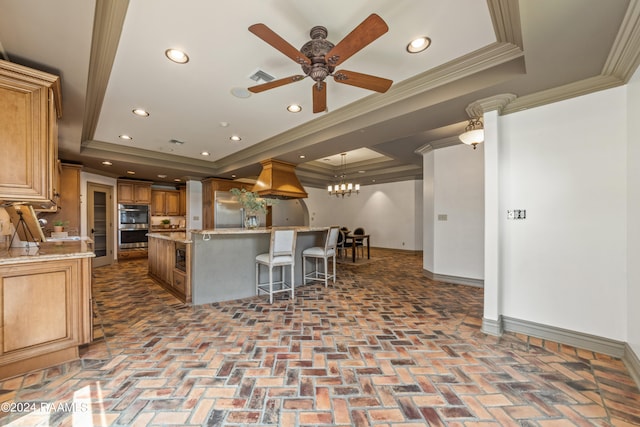 kitchen featuring ceiling fan with notable chandelier, a raised ceiling, a kitchen island with sink, and crown molding