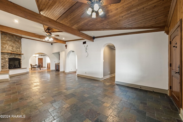 unfurnished living room with vaulted ceiling with beams, ceiling fan, wooden ceiling, and a stone fireplace