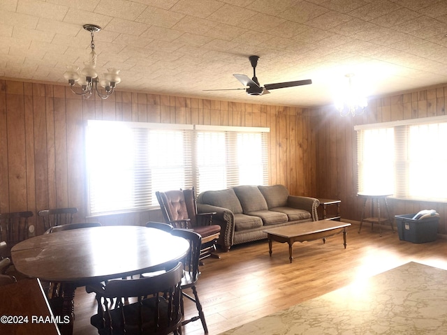 dining room featuring ceiling fan with notable chandelier, wood-type flooring, a healthy amount of sunlight, and wooden walls