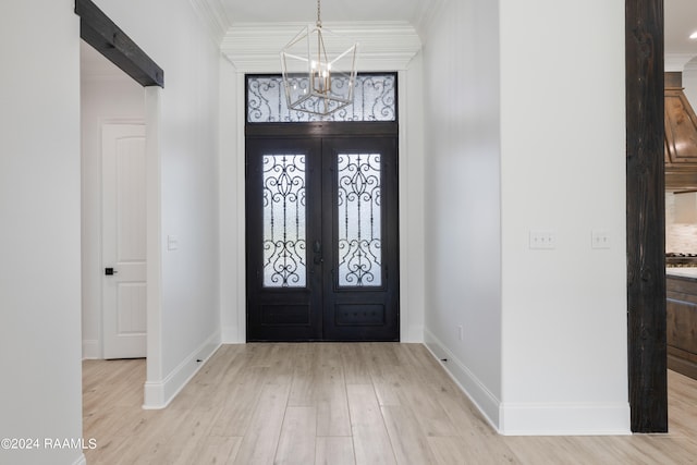 foyer with an inviting chandelier, french doors, ornamental molding, and light wood-type flooring