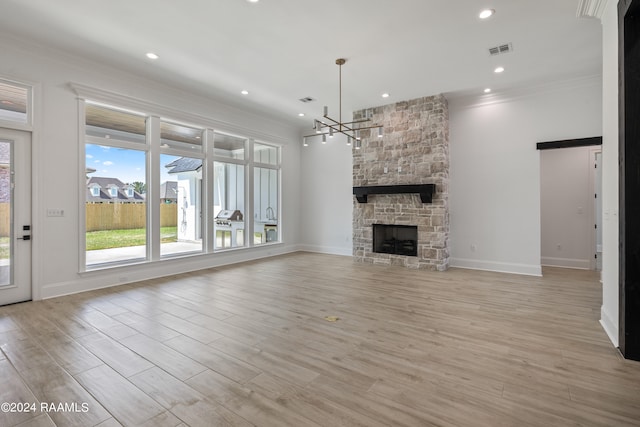 unfurnished living room featuring a fireplace, crown molding, an inviting chandelier, and light wood-type flooring