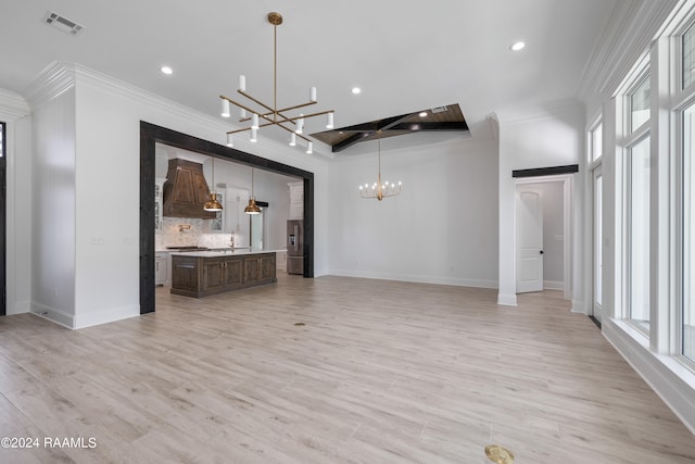 unfurnished living room featuring a barn door, light wood-type flooring, a notable chandelier, sink, and ornamental molding