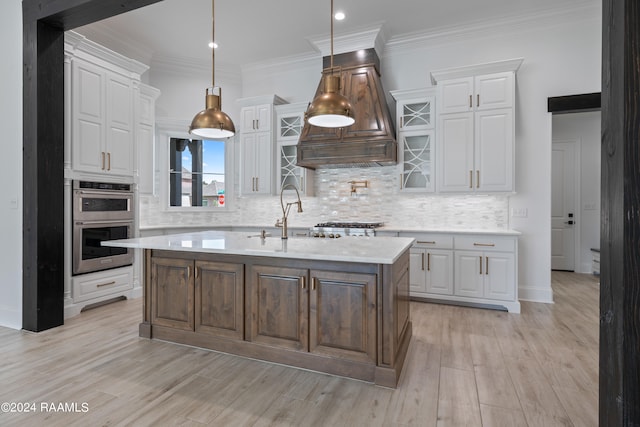 kitchen with an island with sink, white cabinets, sink, light hardwood / wood-style floors, and appliances with stainless steel finishes