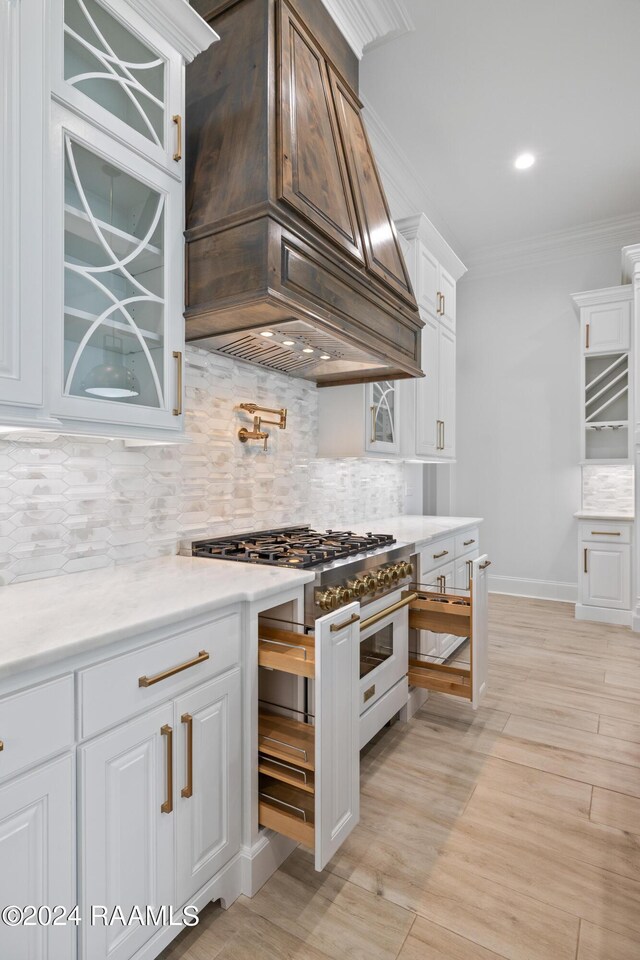 kitchen featuring light hardwood / wood-style floors, decorative backsplash, crown molding, custom exhaust hood, and white cabinets