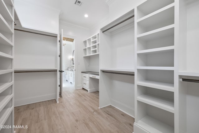 spacious closet with light hardwood / wood-style flooring and built in desk