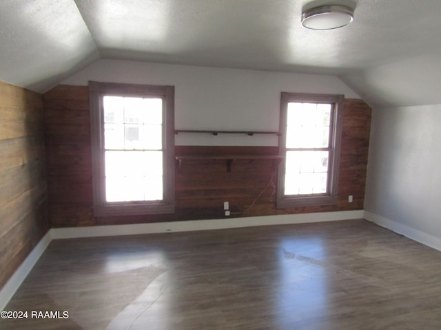 additional living space with wooden walls, dark hardwood / wood-style floors, a textured ceiling, and vaulted ceiling