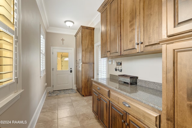 kitchen featuring stone counters, light tile patterned floors, ornamental molding, and a wealth of natural light