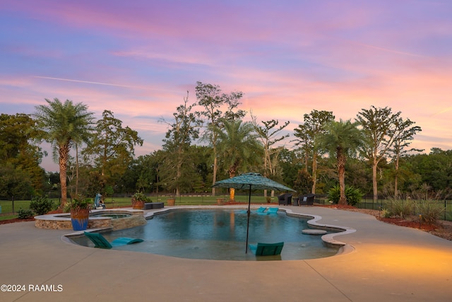 pool at dusk featuring a patio area and an in ground hot tub