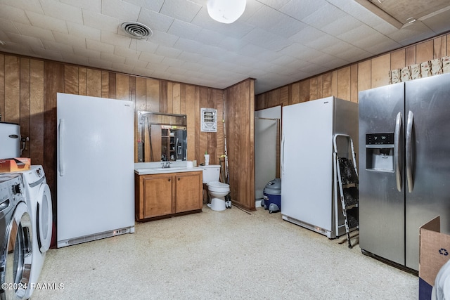 kitchen with wooden walls, washing machine and dryer, white fridge, and stainless steel fridge