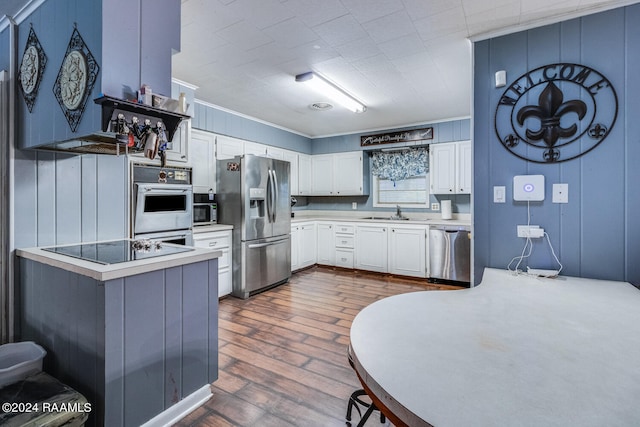 kitchen with white cabinets, kitchen peninsula, appliances with stainless steel finishes, dark hardwood / wood-style flooring, and ornamental molding