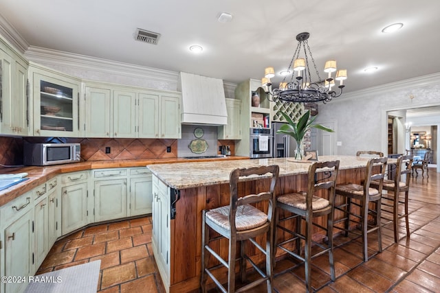 kitchen with a center island, a notable chandelier, custom exhaust hood, appliances with stainless steel finishes, and ornamental molding