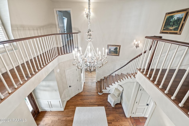 stairway with a towering ceiling, hardwood / wood-style floors, a chandelier, and plenty of natural light