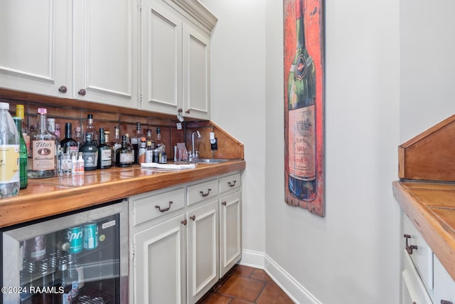 bar with dark tile patterned flooring, white cabinets, wine cooler, wooden counters, and sink