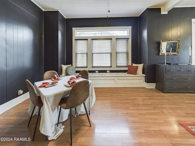 dining room with ornamental molding, light wood-type flooring, wood walls, and beam ceiling