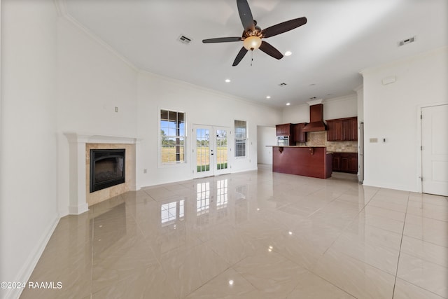 unfurnished living room with ceiling fan, crown molding, french doors, and a tile fireplace