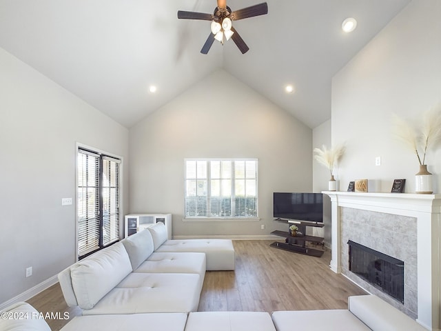 living room with high vaulted ceiling, ceiling fan, light wood-type flooring, and a tile fireplace