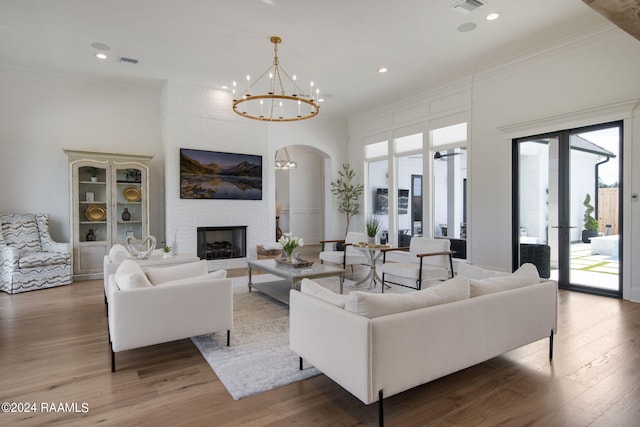 living room featuring an inviting chandelier, hardwood / wood-style flooring, ornamental molding, and a large fireplace