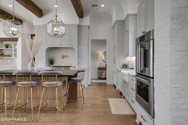 kitchen with a breakfast bar, pendant lighting, light wood-type flooring, beam ceiling, and double oven