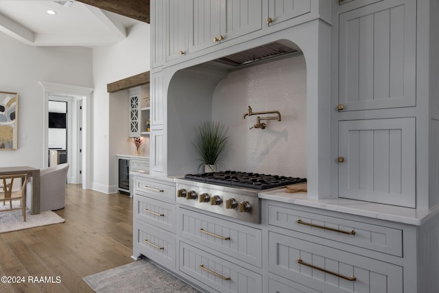 kitchen featuring light stone counters, beam ceiling, stainless steel gas cooktop, beverage cooler, and hardwood / wood-style floors