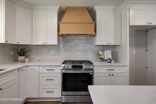 kitchen featuring stainless steel gas range, custom range hood, and white cabinetry