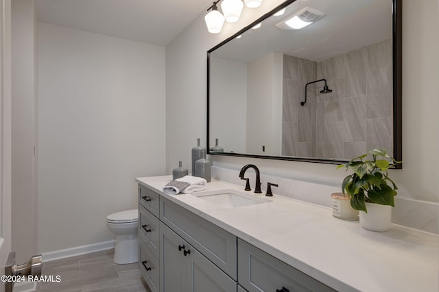 bathroom with a tile shower, wood-type flooring, vanity, and toilet