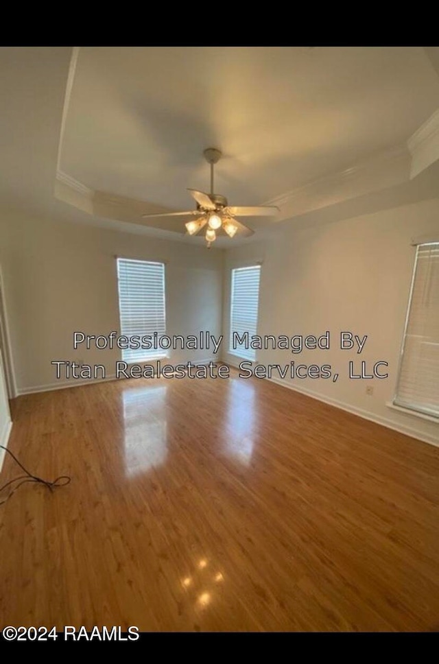 empty room featuring a raised ceiling, crown molding, hardwood / wood-style floors, and ceiling fan