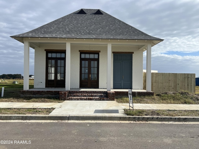 view of front of property featuring fence, brick siding, a shingled roof, french doors, and a porch