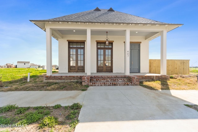 doorway to property with a shingled roof, covered porch, french doors, and brick siding