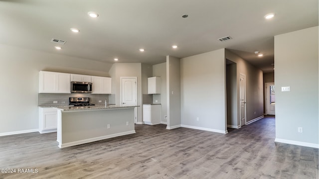 kitchen featuring white cabinets, light wood-type flooring, a center island with sink, appliances with stainless steel finishes, and light stone countertops