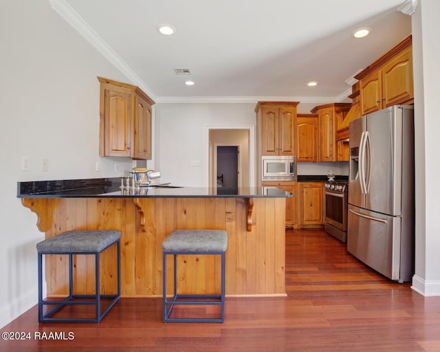 kitchen with kitchen peninsula, a kitchen breakfast bar, appliances with stainless steel finishes, dark hardwood / wood-style flooring, and ornamental molding