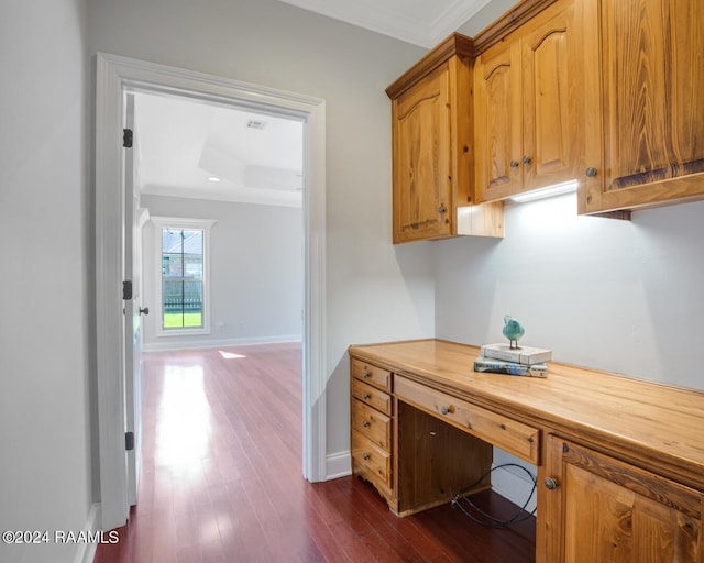 office featuring a raised ceiling, built in desk, dark wood-type flooring, and crown molding