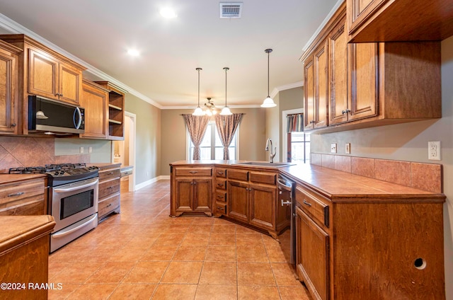 kitchen featuring kitchen peninsula, stainless steel appliances, crown molding, decorative light fixtures, and sink