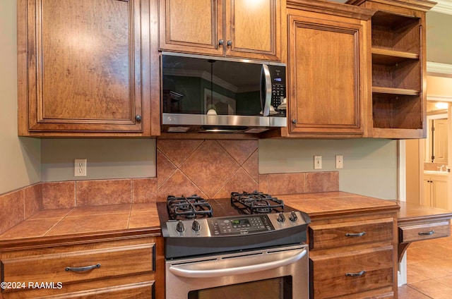 kitchen featuring tile counters, light tile patterned flooring, decorative backsplash, stainless steel appliances, and ornamental molding