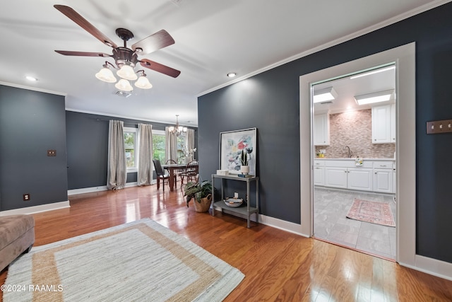 living room featuring light hardwood / wood-style flooring, ornamental molding, and ceiling fan with notable chandelier