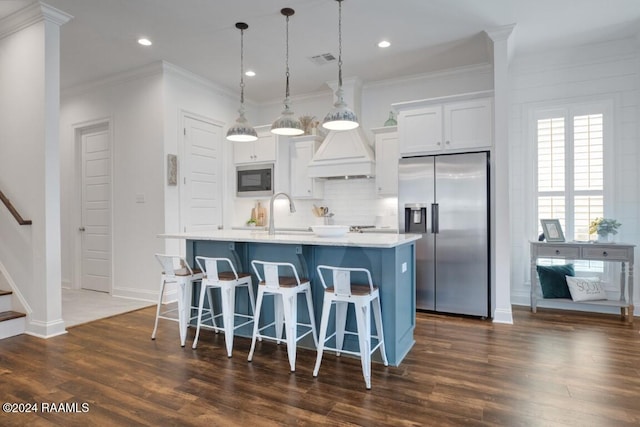 kitchen featuring appliances with stainless steel finishes, white cabinets, dark hardwood / wood-style flooring, pendant lighting, and a kitchen island with sink