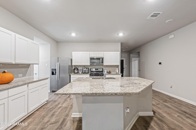 kitchen featuring stainless steel appliances, a center island with sink, white cabinetry, tasteful backsplash, and light stone countertops