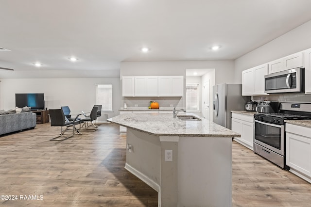 kitchen with white cabinetry, appliances with stainless steel finishes, an island with sink, and light hardwood / wood-style flooring