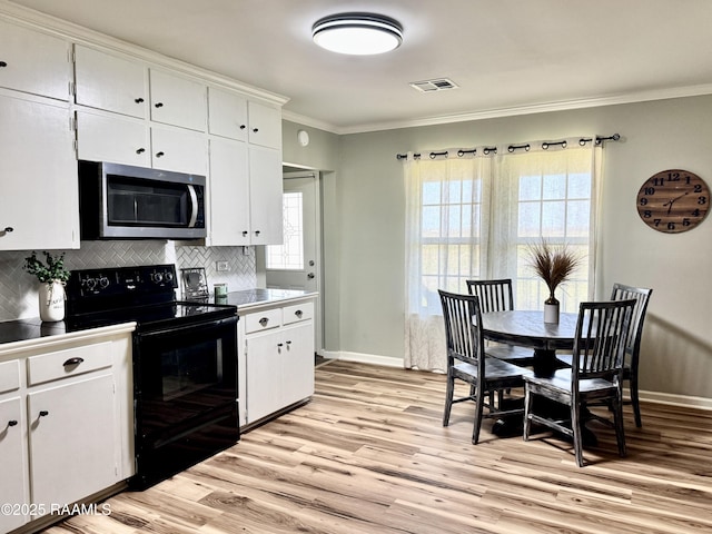 kitchen with black / electric stove, light wood-style flooring, ornamental molding, decorative backsplash, and stainless steel microwave