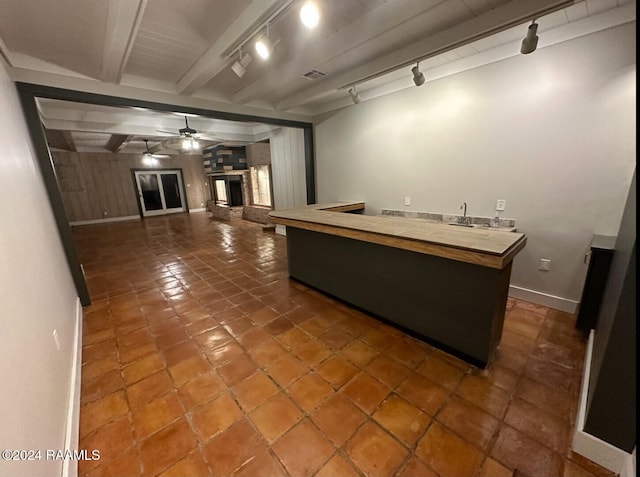 kitchen featuring dark tile patterned flooring, a fireplace, ceiling fan, beam ceiling, and track lighting