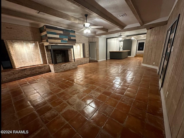 unfurnished living room with beamed ceiling, ceiling fan, a fireplace, and dark tile patterned flooring