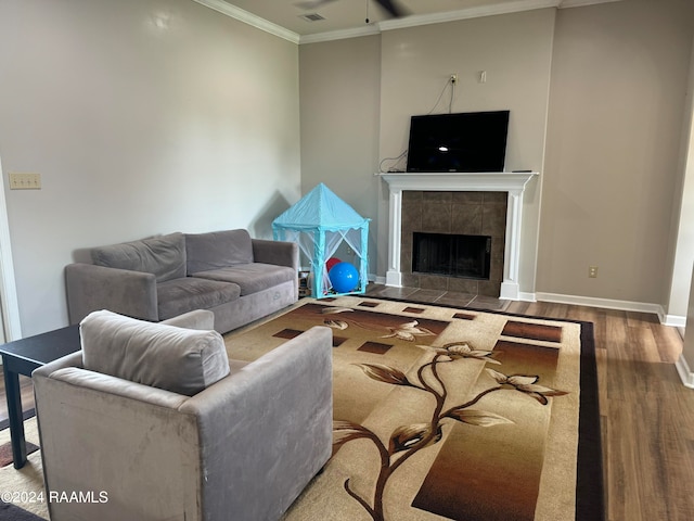 living room featuring ceiling fan, crown molding, hardwood / wood-style floors, and a tile fireplace